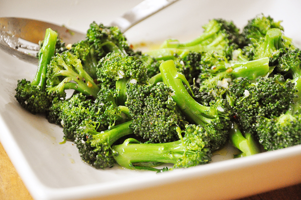Spicy steamed broccoli with garlic, chilli flakes and lemon juice on a white plate.