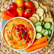 A platter with red pepper hummus, crudites and crackers.