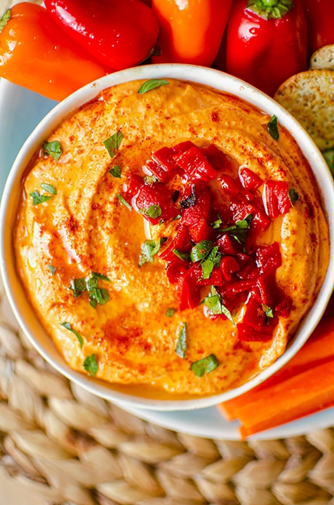 Closeup of hummus in a bowl with red peppers scattered on top