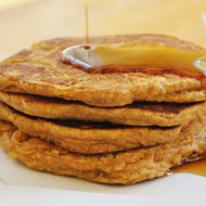 A stack of whole wheat pumpkin pancakes with a drizzle of maple syrup
