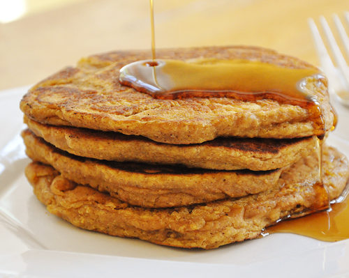 A stack of whole wheat pumpkin pancakes with a drizzle of maple syrup