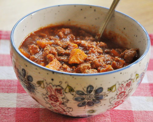 Slow cooker sweet potato chili in a floral bowl on a red checked napkin.