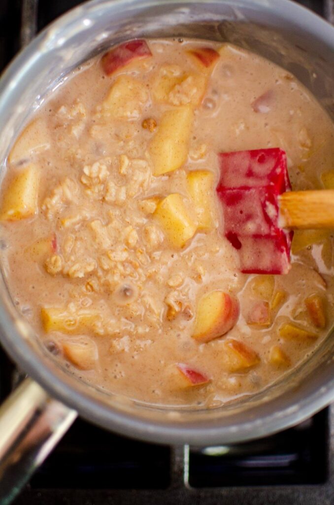 Apple oatmeal being stirred in a pot on the stovetop.