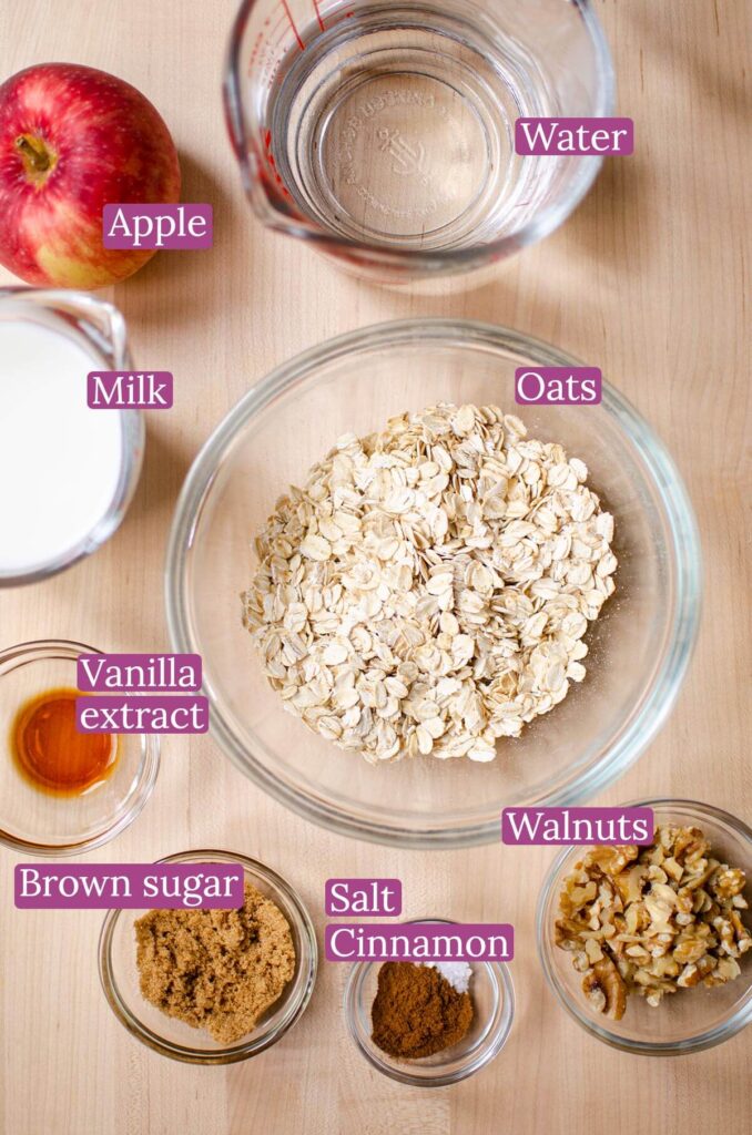Ingredients for oatmeal including oats, brown sugar, vanilla extract, cinnamon, salt, apple, walnuts, water and milk in small glass bowls.