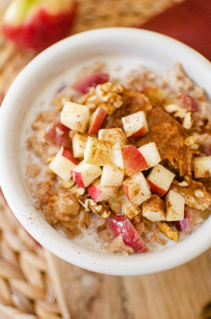 A bowl of oatmeal with chopped fresh apples, walnuts and peanut butter on top.
