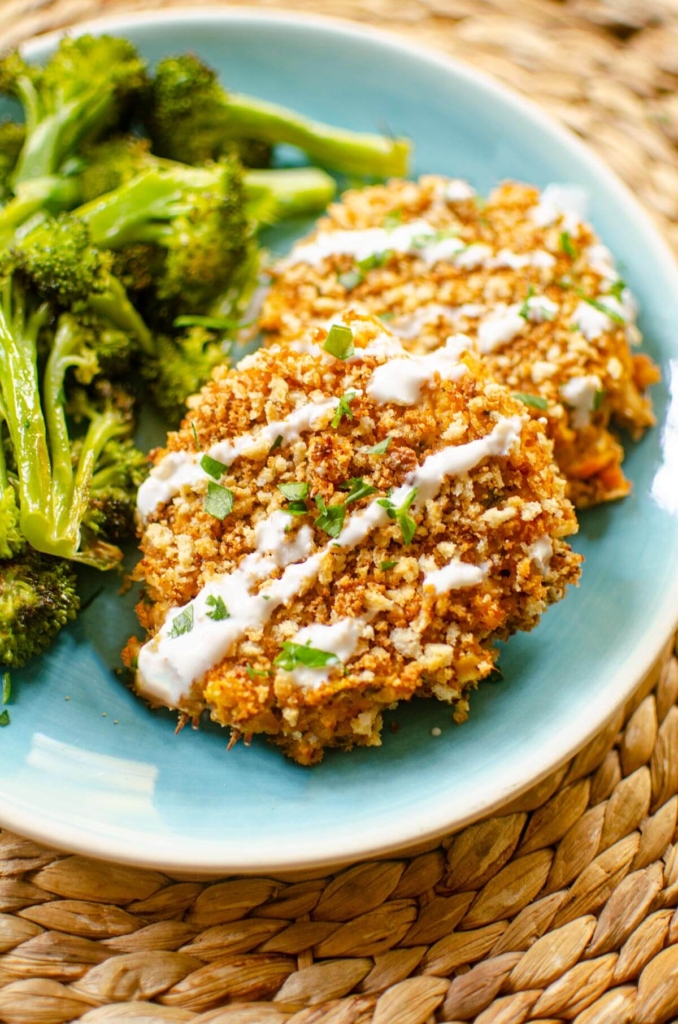 A serving of salmon patties on a plate with broccoli, drizzled with tartar sauce.