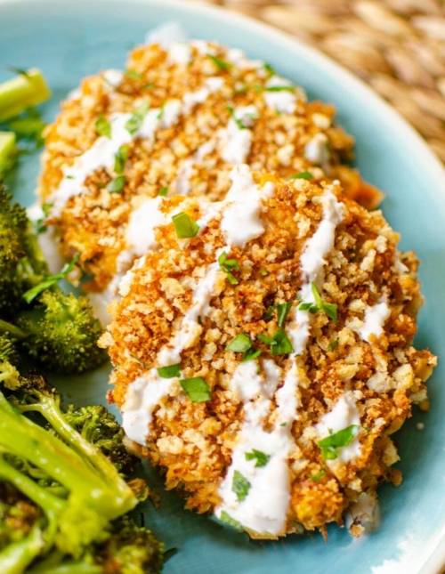 Closeup of a serving of salmon patties on a plate with broccoli and tartar sauce.