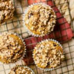 Closeup of banana pumpkin muffins on a cooling rack with a burgundy napkin.