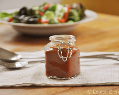 A jar of roasted red pepper salad dressing with a green salad in the background