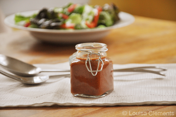 A jar of roasted red pepper salad dressing with a green salad in the background