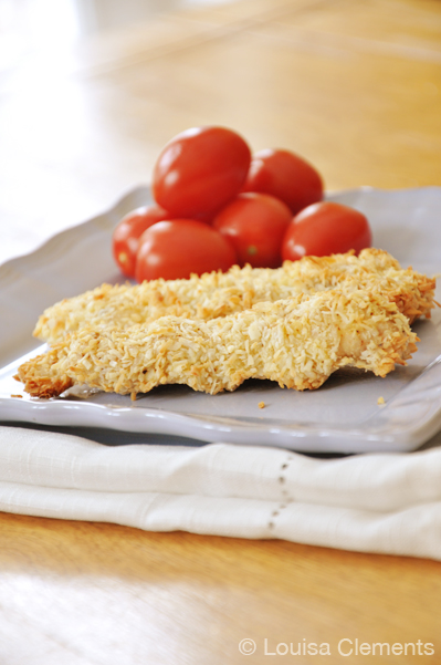 Coconut crusted chicken strips on a plate with cherry tomatoes