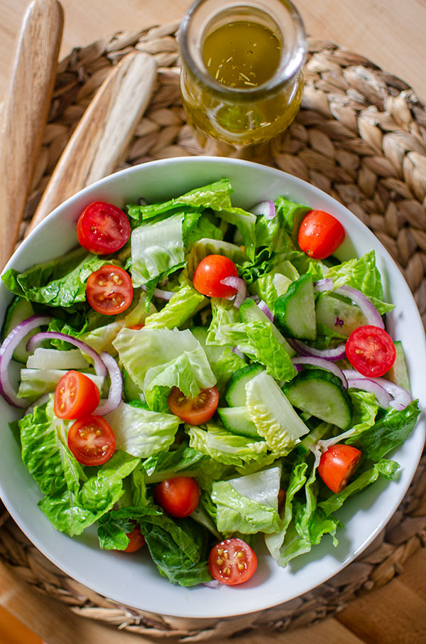 A classic green salad in a bowl with cherry tomatoes and a jar of salad dressing on the side.