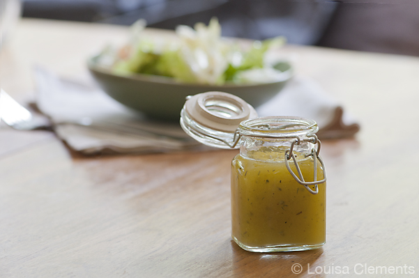 Old photo of white balsamic vinaigrette in a small jar with a bowl of salad in the background from the recipe posted in 2012.
