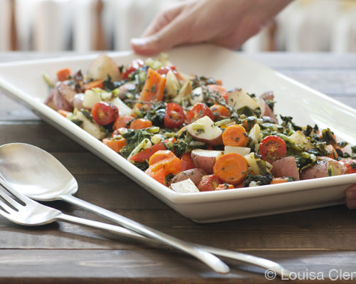 Two hands placing a plate of summer roasted vegetables on a table