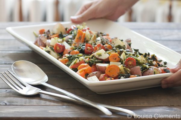 Two hands placing a plate of summer roasted vegetables on a table