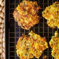 Cooked fritters on a wire rack on a baking sheet.