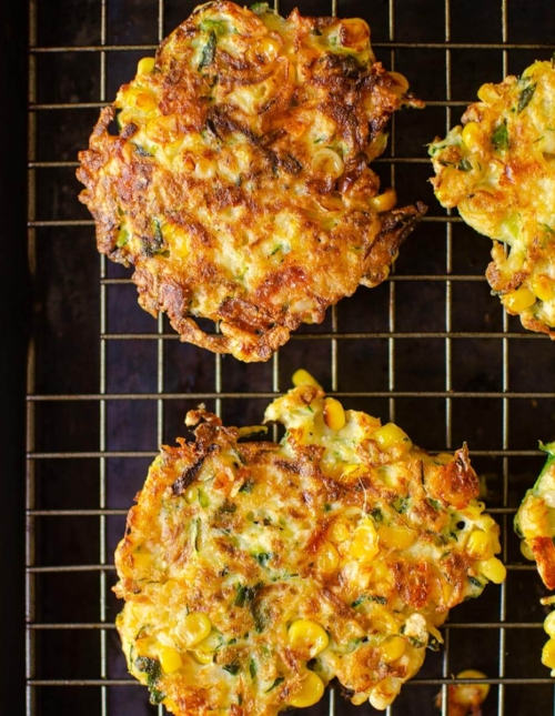 Cooked fritters on a wire rack on a baking sheet.