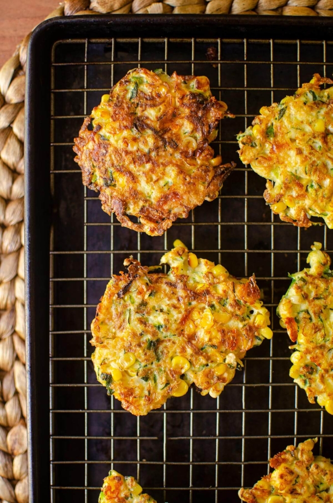 Cooked fritters on a wire rack on a baking sheet.