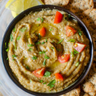 Melitzanosalata in a bowl with chopped tomatoes and parsley sprinkled on top with crackers on the side.