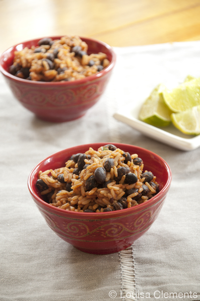Two small red bowls filled with rice and beans with a small plate of sliced limes.