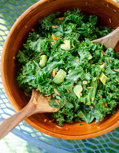 Kale avocado salad in a wooden bowl on an outdoor table.