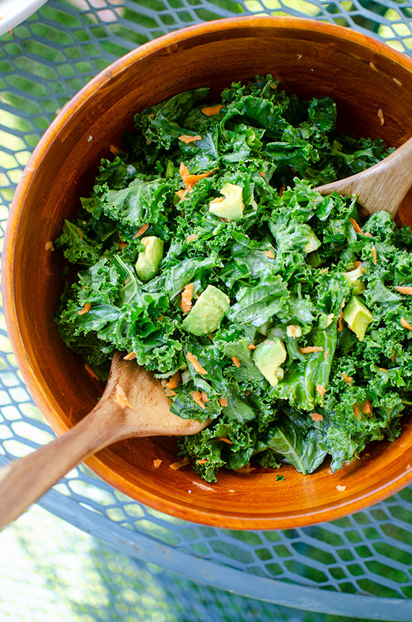 Kale avocado salad in a wooden bowl on an outdoor table.