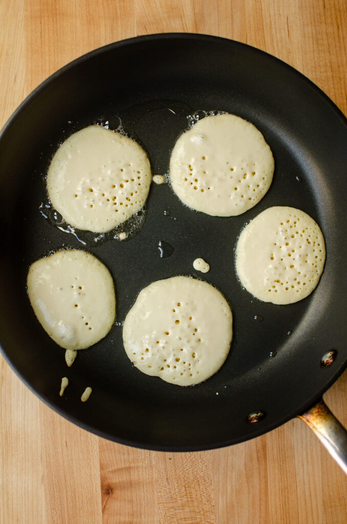 The batter of small pancakes in a non stick frying pan.