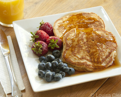 A plate of diner style pancakes with blueberries, strawberries and a glass of orange juice