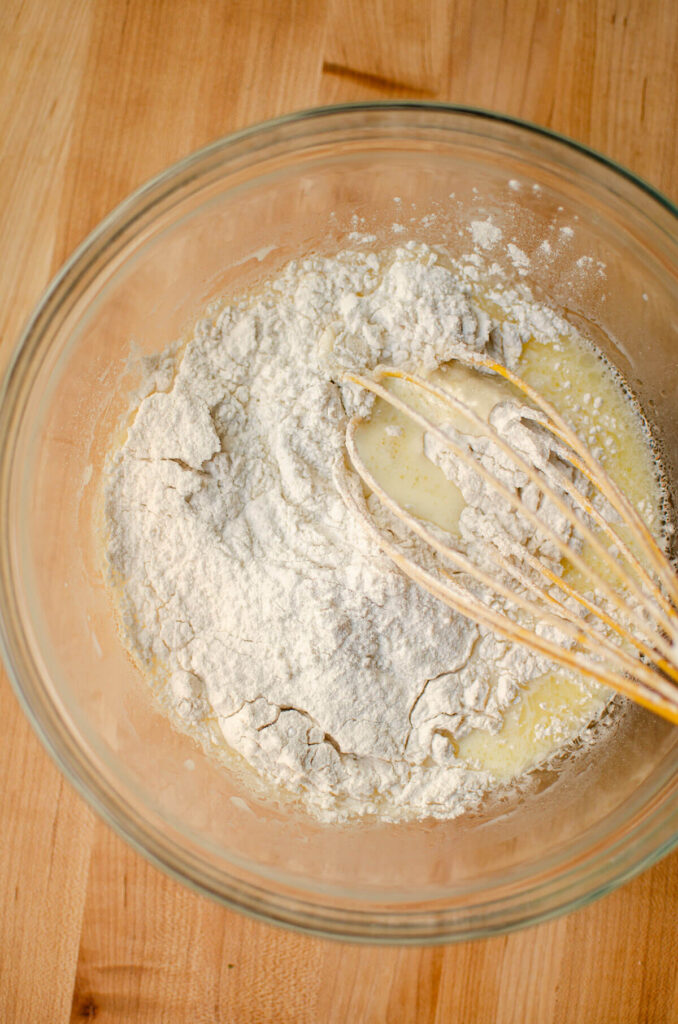 Dry and wet ingredients being whisked together in a glass bowl.
