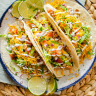 Three chicken tacos on a plate with all of the toppings; lettuce, tomatoes, cheese and sour cream.