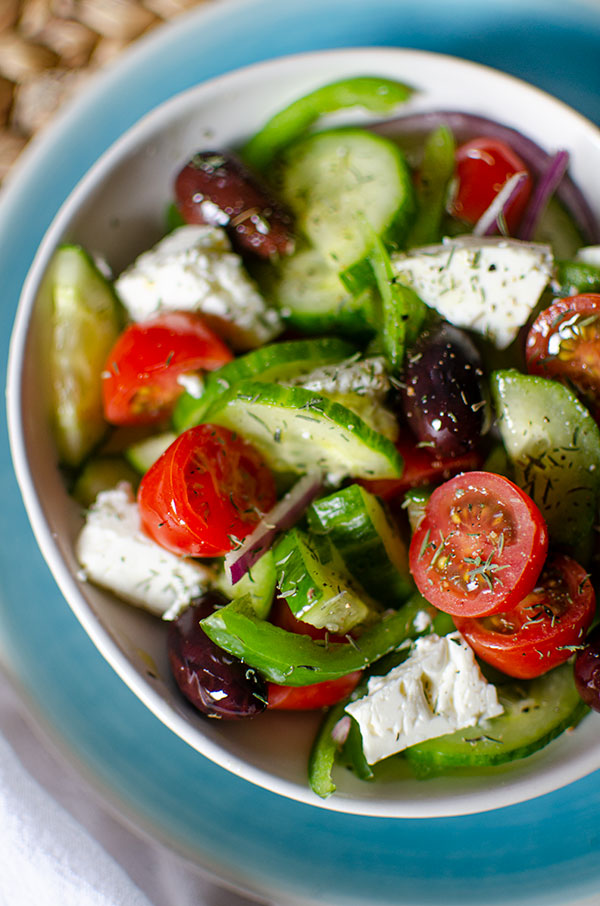 Greek salad in a white bowl with dried thyme sprinkled on top.