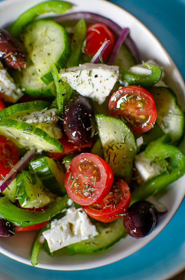 Close up of Greek salad in a white bowl with dried thyme sprinkled on top.