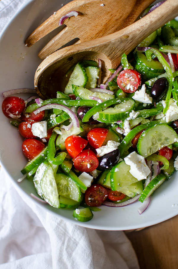 Greek salad in a large white bowl with wooden salad spoons and a white napkin