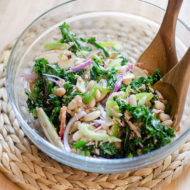 Kale and white bean salad in a glass bowl with wooden salad spoons