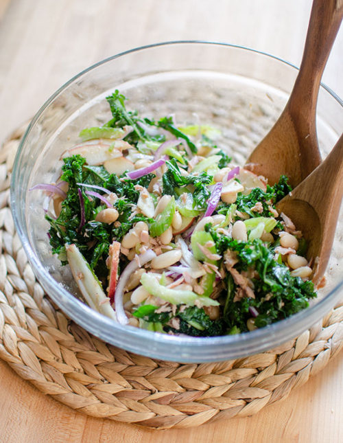 Kale and white bean salad in a glass bowl with wooden salad spoons