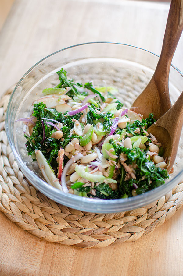 Kale and white bean salad in a glass bowl with wooden salad spoons