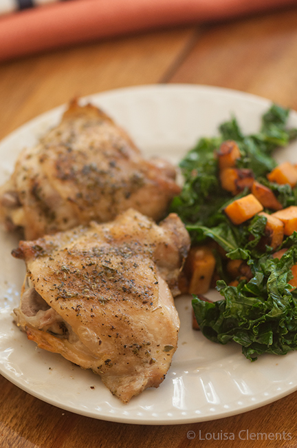 closeup of perfectly roasted chicken thighs on a plate with sauteed kale and sweet potatoes