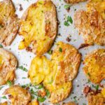 Closeup of crispy potatoes sprinkled with parsley on a baking sheet.