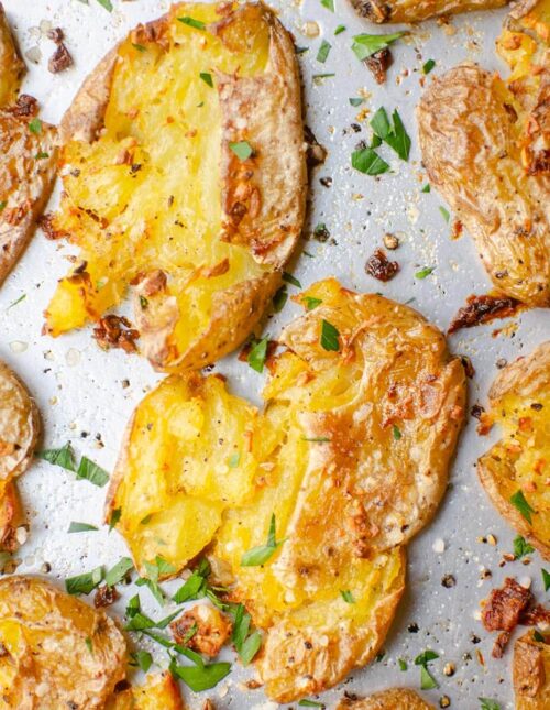 Closeup of crispy potatoes sprinkled with parsley on a baking sheet.