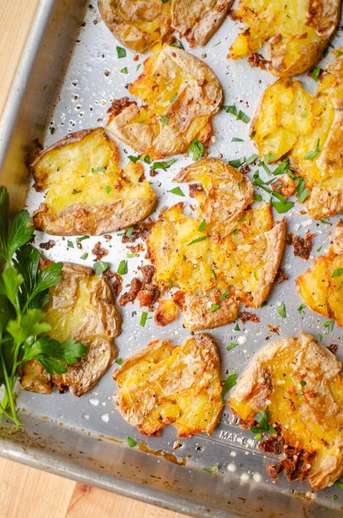 Closeup of crispy smashed potatoes on a baking sheet with parsley sprinkled over top.