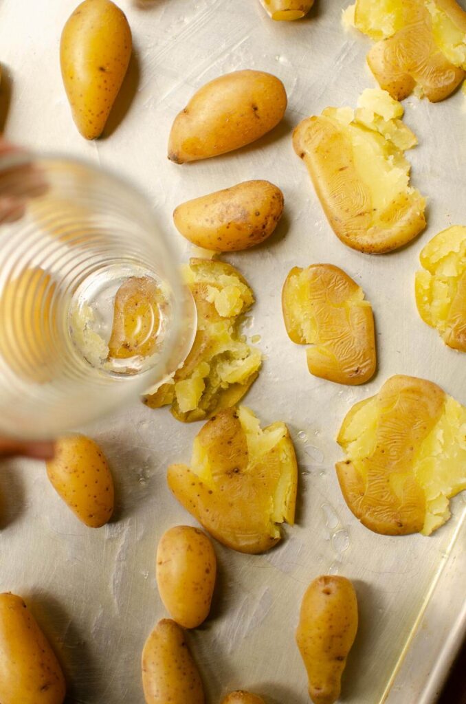 Potatoes being smashed with the bottom of a glass on a baking sheet.
