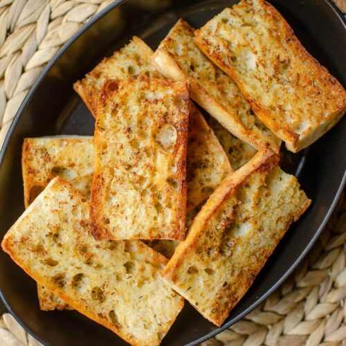 Closeup of finished garlic bread in a black dish.