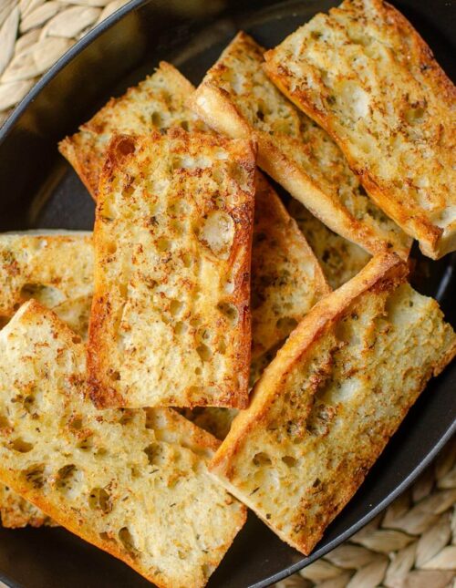 Closeup of finished garlic bread in a black dish.
