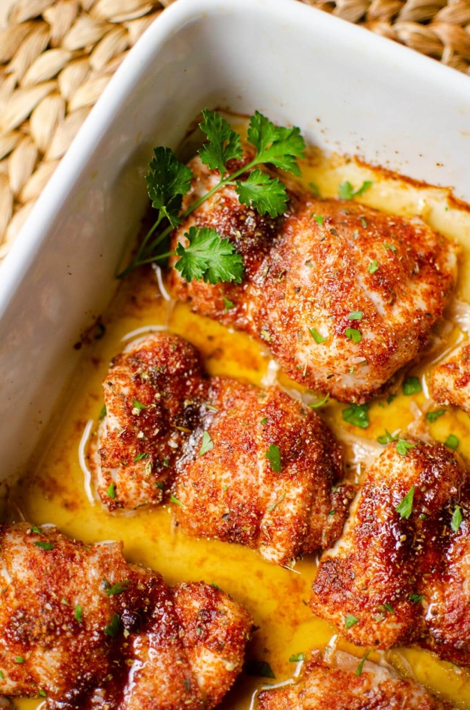 Closeup of cooked chicken thighs in a white casserole dish.