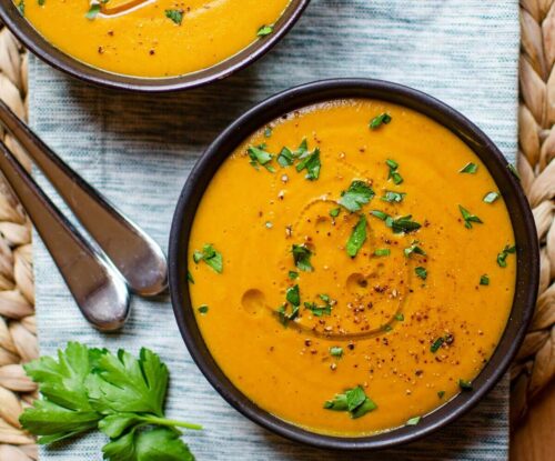 Closeup of two bowls of carrot lentil soup on a striped napkin.