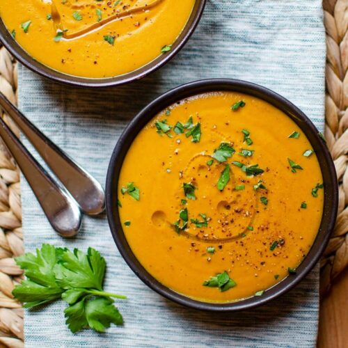 Closeup of two bowls of carrot lentil soup on a striped napkin.