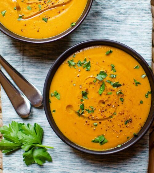 Closeup of two bowls of carrot lentil soup on a striped napkin.