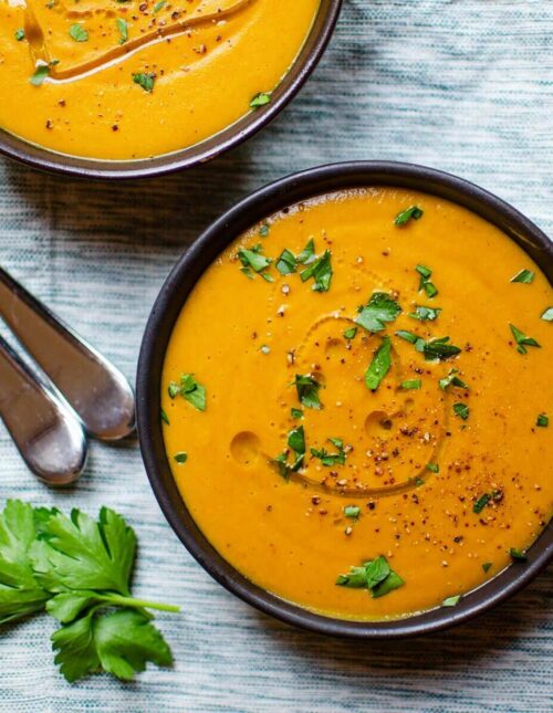 Closeup of two bowls of carrot lentil soup on a striped napkin.