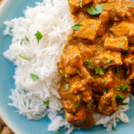 A plate with rice and slow cooker butter chicken with cilantro sprinkled on top
