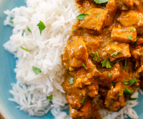 A plate with rice and slow cooker butter chicken with cilantro sprinkled on top